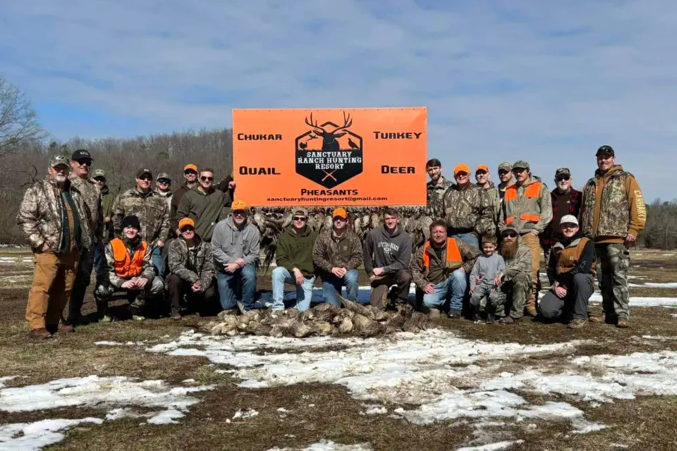Group of hunters gathered in front of the lodge sign at Sanctuary Ranch in Mount Pleasant, Arkansas after a successful hunt