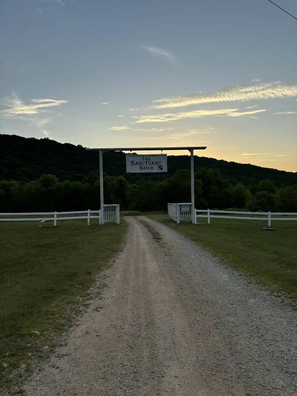 Entrance to The Sanctuary Ranch hunting lodge in Arkansas at sunset with welcome sign and gravel drive